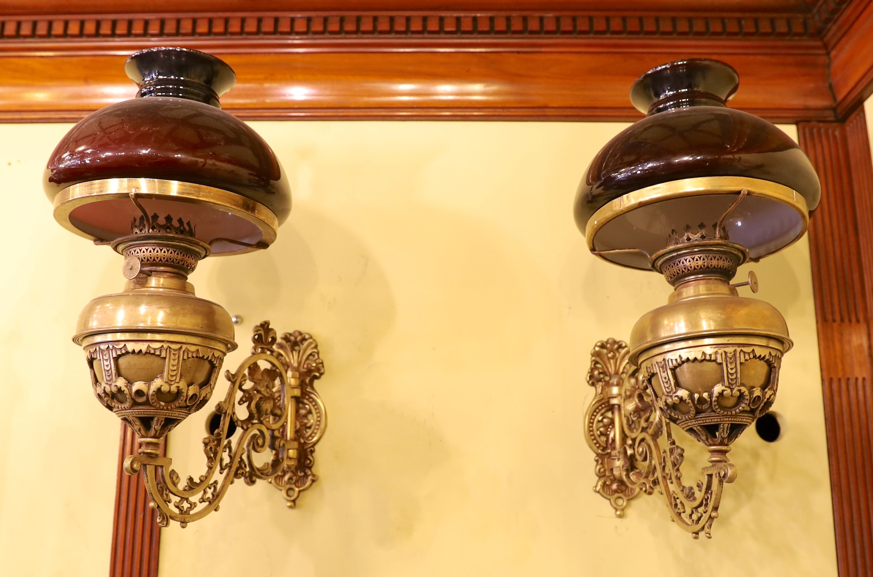 A pair of Victorian brass wall mounted oil lamps, with swivelling foliate pierced branches and aubergine glass shades, height overall 40cm